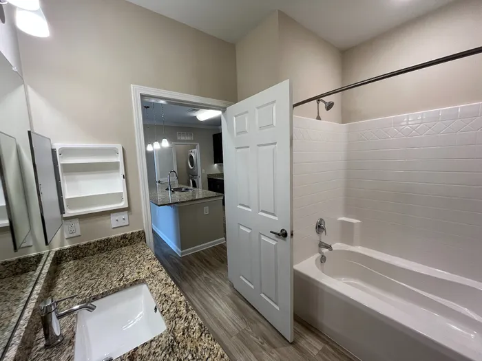 Modern bathroom with elegant granite countertops, a spacious bathtub, and a view into a stylish kitchen.