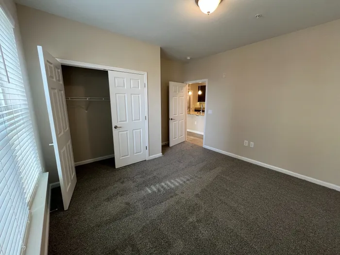 Inviting bedroom with plush carpeting, bright natural light, and convenient closet space, perfect for a relaxing retreat.
