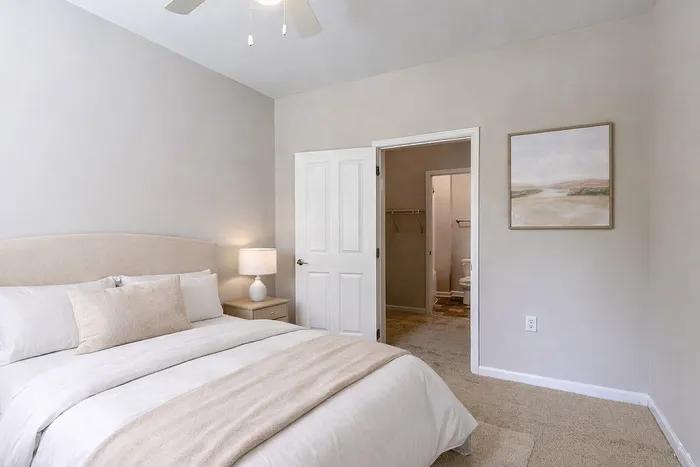 Bright and inviting bedroom with plush bedding, tasteful art, and a view into an ensuite bathroom, ideal for comfort and relaxation.