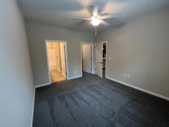 Spacious bedroom featuring plush carpeting, ceiling fan, and direct access to a bright bathroom.