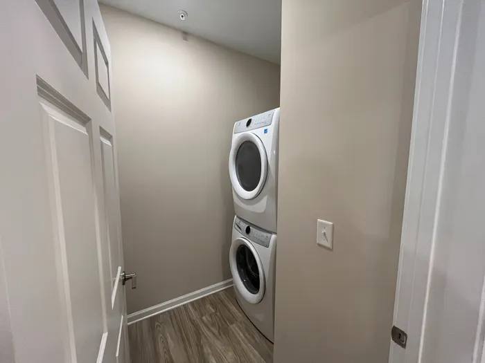 Modern apartment laundry area featuring a sleek stackable washer and dryer set, complemented by elegant wood flooring.