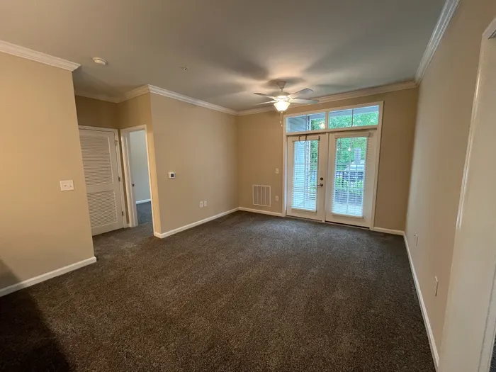 Elegant living room with plush carpet, ceiling fan, and bright French doors opening to a scenic view, perfect for relaxation.
