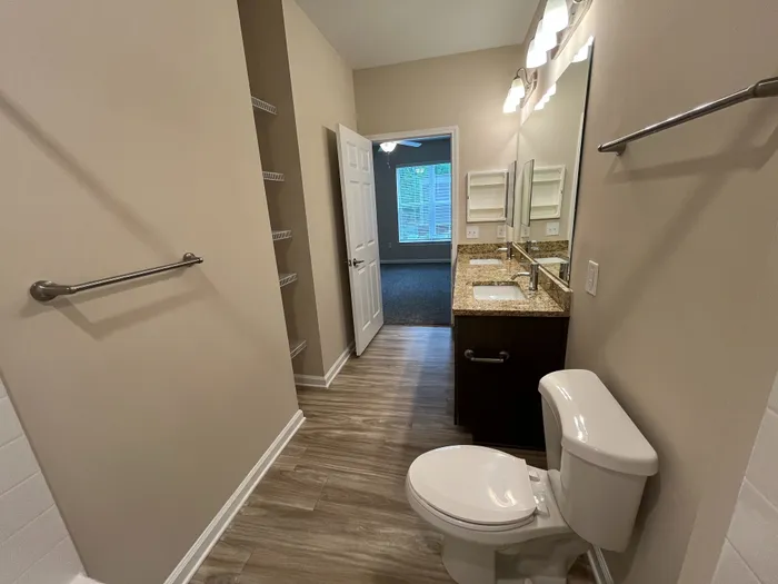 Bright and modern bathroom with granite countertop, dual sinks, and elegant lighting, leading to a cozy bedroom with large windows.