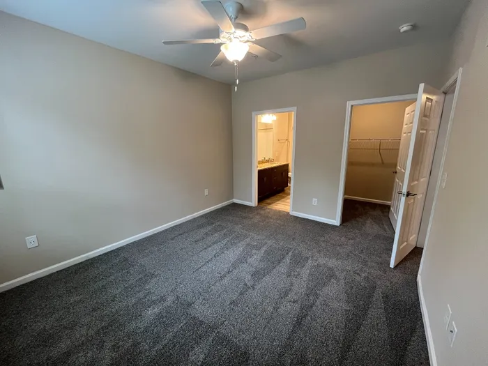 Spacious bedroom with plush carpeting, bright ceiling fan, and en-suite bathroom with elegant vanity and large walk-in closet.
