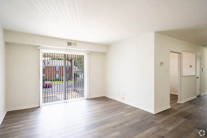 Bright living area with sleek wooden floors and large sliding glass doors opening to a serene outdoor view.