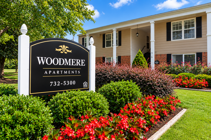 Charming Woodmere Apartments surrounded by lush greenery and vibrant flowers, highlighting a welcoming environment.