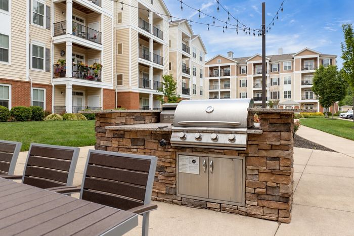 Inviting outdoor community area with a sleek stone barbecue grill, surrounded by modern apartment buildings with balconies and lush greenery.