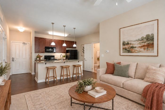 Inviting open-concept living room with cozy beige sofa, modern kitchen with island counter, and stylish decor.
