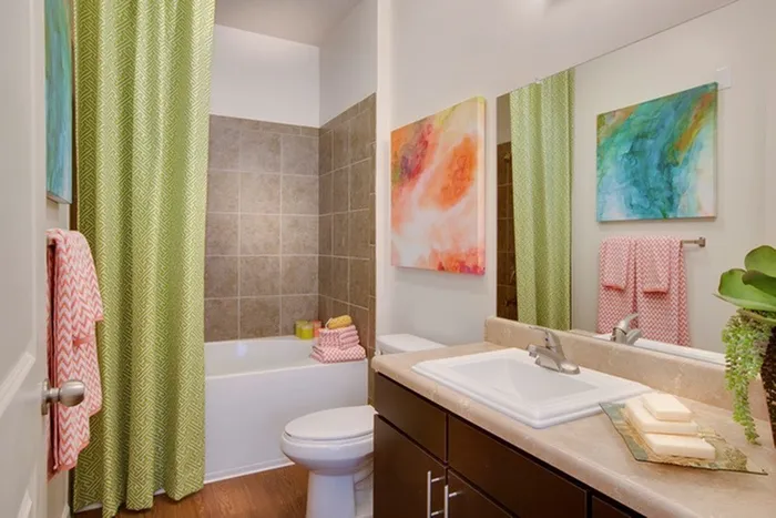 Photo of bathroom showing wood-style plank flooring, modern sink with modern cabinetry beneath, toilet, and bathtub with shower curtain.