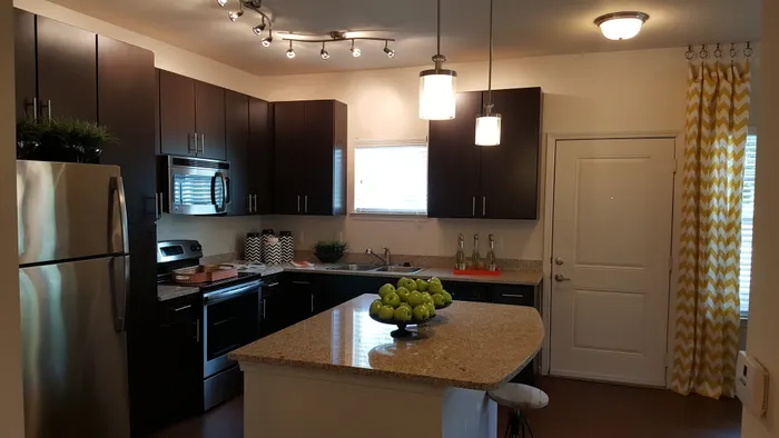 Photo of kitchen with large island, granite counter-tops, modern cabinetry, microwave, electric stove, dishwasher, refrigerator, and double sided sink, from a different angle, showing it next to the entry door.