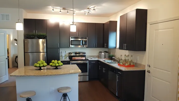 Photo of kitchen with large island, granite counter-tops, modern cabinetry, microwave, electric stove, dishwasher, refrigerator, and double sided sink, from a different angle, showing seating at the island and both pendant and track lightin