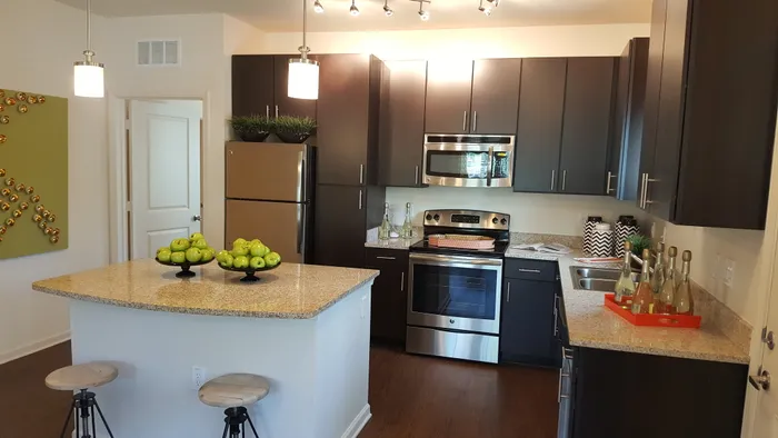 Photo of kitchen with large island, granite counter-tops, modern cabinetry, microwave, electric stove, dishwasher, refrigerator, and double sided sink, from a different angle, showing seating at the island and both pendant and track lightin