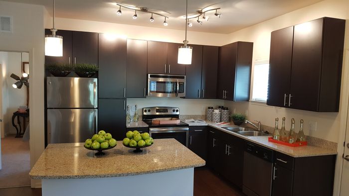 Photo of kitchen with large island, granite counter-tops, modern cabinetry, microwave, electric stove, dishwasher, refrigerator, and double sided sink.