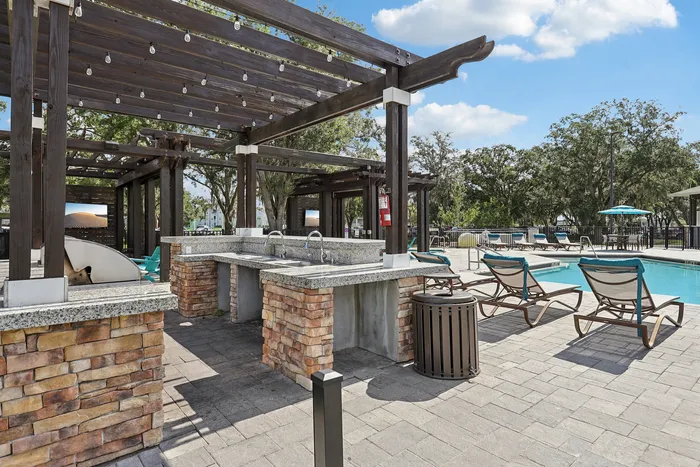 Luxurious outdoor pool area with stylish pergola and modern lounge chairs, perfect for relaxation under a sunny sky.