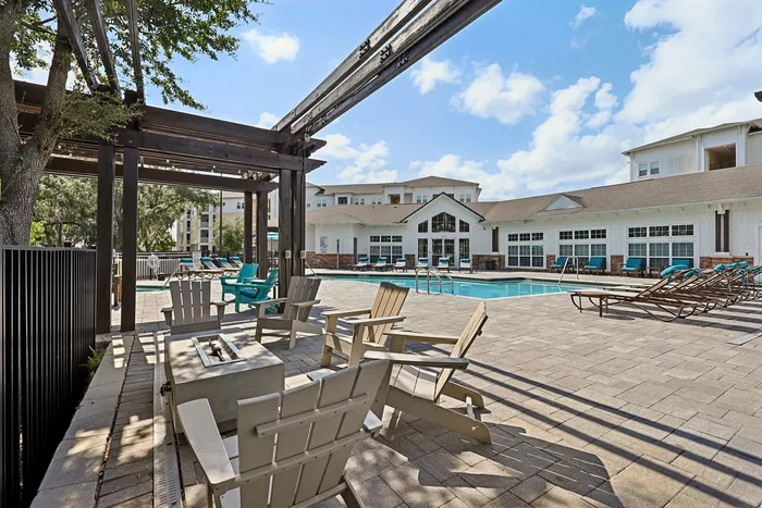 Luxurious apartment complex with inviting pool and stylish outdoor seating under pergola, perfect for relaxation.