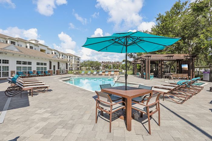 Luxurious apartment complex pool area featuring relaxing lounge chairs, vibrant turquoise umbrellas, and a spacious sunlit deck.