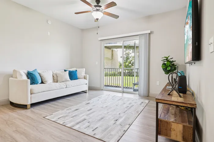Bright and welcoming living room with a cozy white sofa, modern decor, and large sliding glass door leading to a serene outdoor space.