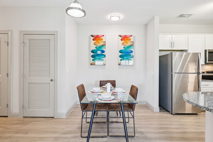 Modern dining area with a glass table for four, vibrant abstract wall art, and a sleek stainless steel kitchen in a chic apartment.