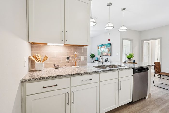 Modern kitchen with elegant granite countertops, stylish pendant lighting, and open-concept design seamlessly connecting to a cozy living area, ideal for contemporary living.