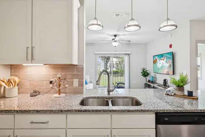 Elegant kitchen with granite countertops, modern pendant lighting, and an open view into a stylish living room with large windows and a scenic outdoor vista.