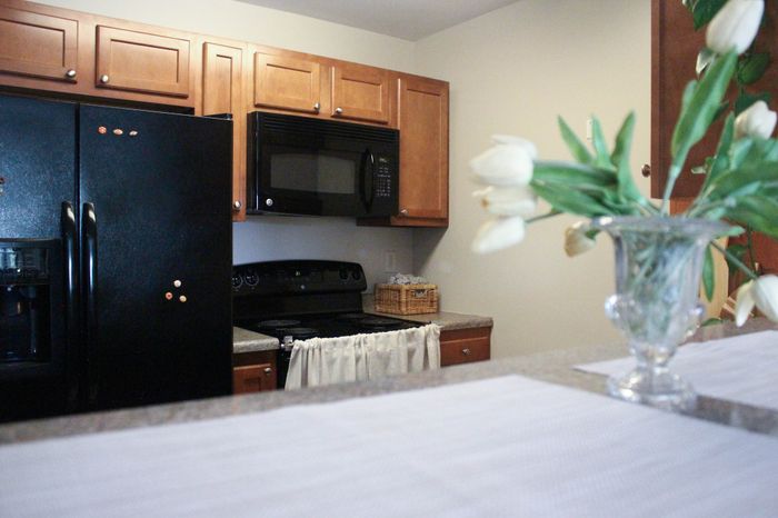 Inviting kitchen with warm wooden cabinets, sleek black appliances, and elegant floral decor on the counter.