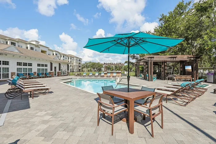 Inviting pool area with turquoise lounge chairs and umbrellas, surrounded by modern architecture and lush greenery, perfect for relaxation.