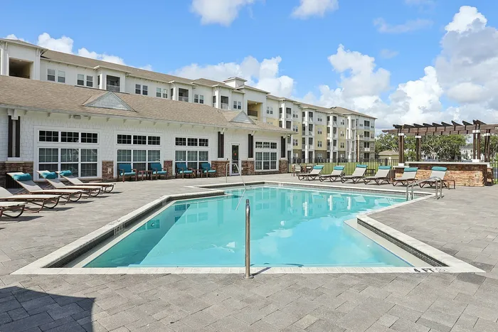 Luxurious apartment complex showcasing a pristine swimming pool surrounded by stylish loungers and modern architecture under a bright blue sky.