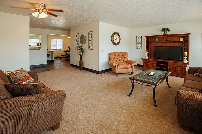 Warm and inviting living room with plush seating, elegant ceiling fan, and stylish decor opening into a well-lit dining area.