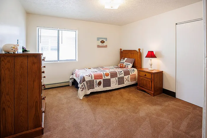 Charming bedroom featuring warm wooden furniture, cozy twin bed with colorful sports-themed quilt, and bright natural lighting.