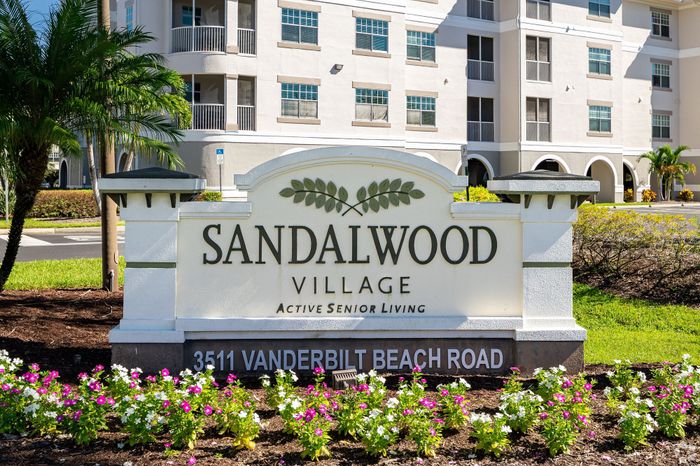 Inviting entrance to Sandalwood Village, showcasing modern senior living with lush landscaping and vibrant flowers.