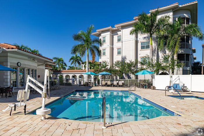Bright and inviting pool area with sun umbrellas, elegant palm trees, and Mediterranean-style architecture, perfect for relaxation.