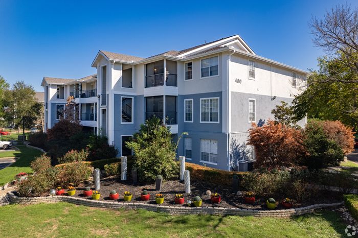 Charming apartment complex with modern design, surrounded by vibrant landscaping and colorful planters under a clear blue sky.