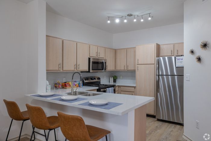 Modern kitchen with sleek stainless steel appliances, elegant light wood cabinetry, and a chic breakfast bar with comfortable brown leather stools.
