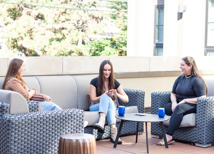 Vibrant outdoor patio with contemporary wicker furniture and three people enjoying a friendly conversation over coffee.