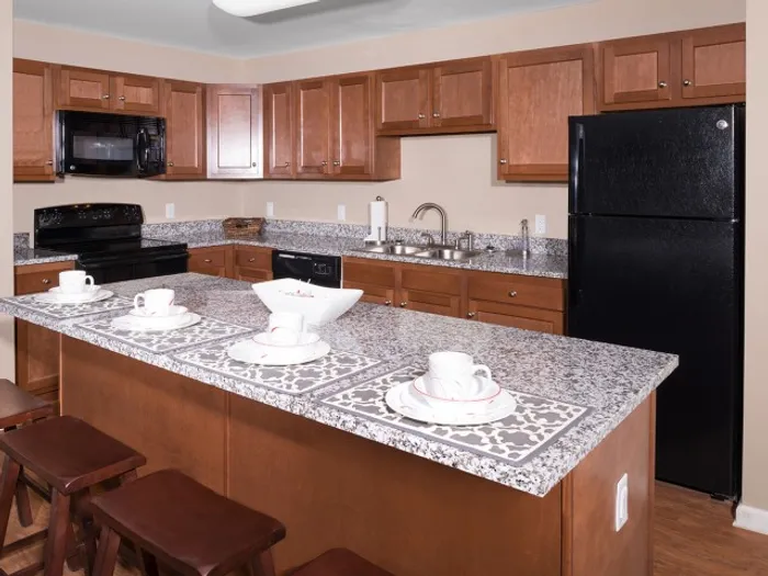 Spacious kitchen with cherry wood cabinets, granite countertops, and black appliances at University Hills Apartments near the University of Toledo