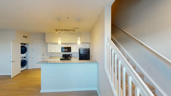 A modern kitchen with granite countertops, pendant lighting, and an adjacent staircase at Ralston Apartments in Downtown Indianapolis, featuring sleek appliances and an in-unit washer and dryer.