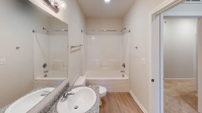 A clean, modern bathroom at Ralston Apartments in Downtown Indianapolis, featuring a granite vanity, a spacious tub and shower combo, and wood-like vinyl flooring.