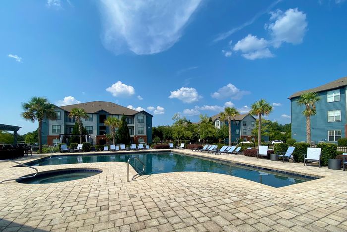 Resort-style pool and sundeck at Eagle Flatts Apartments in Hattiesburg, MS with lounge chairs and palm trees.