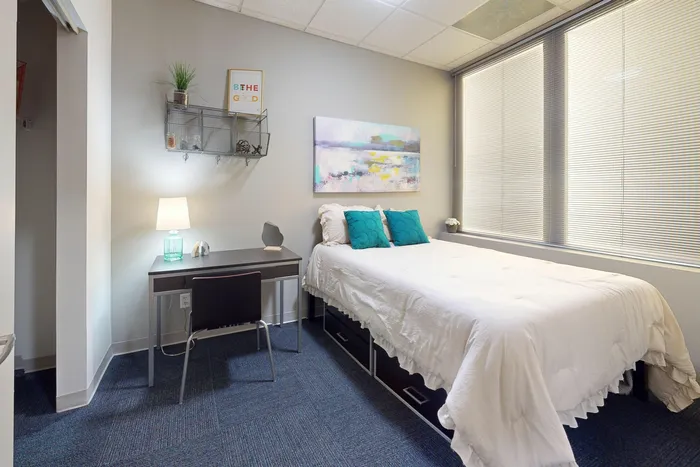 Furnished bedroom featuring a dedicated study area and under-bed storage in University Plaza off-campus apartments near NIU