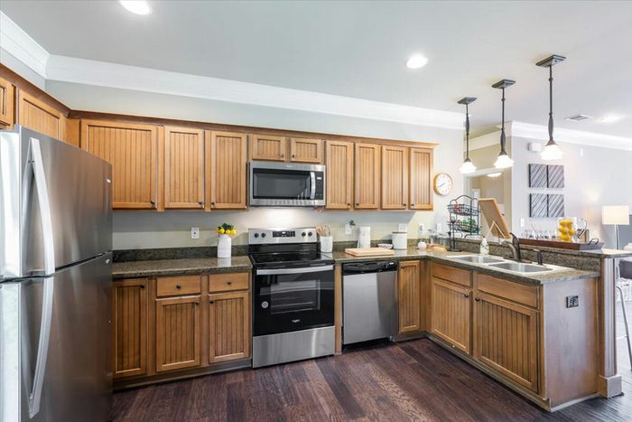 Spacious kitchen at The Cottages of Hattiesburg featuring wood cabinets, granite countertops, and stainless steel appliances, ideal for student living.