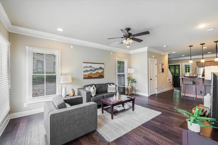 Bright and modern living room at The Cottages of Hattiesburg featuring comfortable seating, hardwood floors, and an open floor plan leading to the kitchen. Perfect for student living.