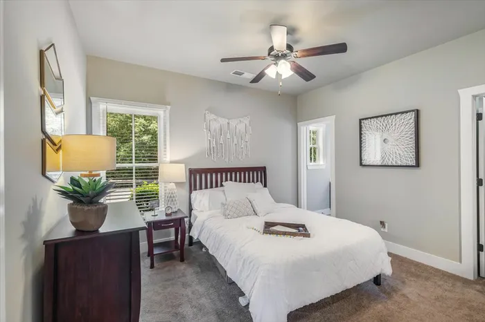 Comfortable and well-lit private bedroom at The Cottages of Hattiesburg featuring a ceiling fan, cozy bed, and modern decor, ideal for student living.