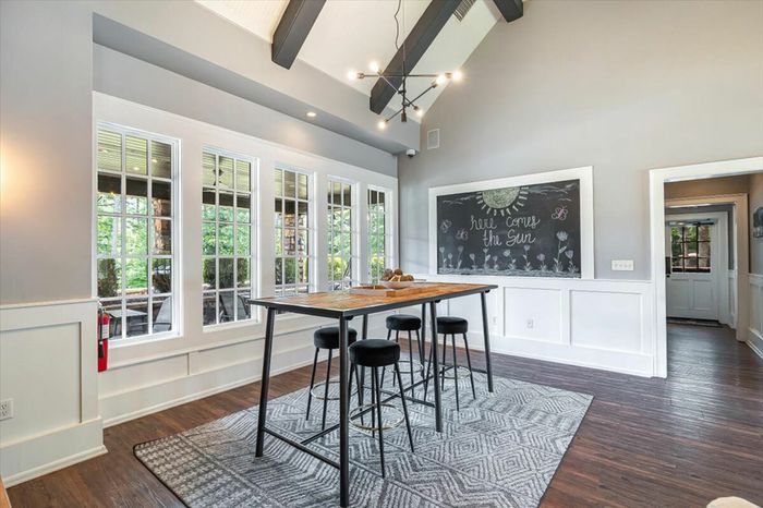 Spacious community area at The Cottages of Hattiesburg featuring large windows, a high table with stools, and a chalkboard wall, perfect for studying or social gatherings.