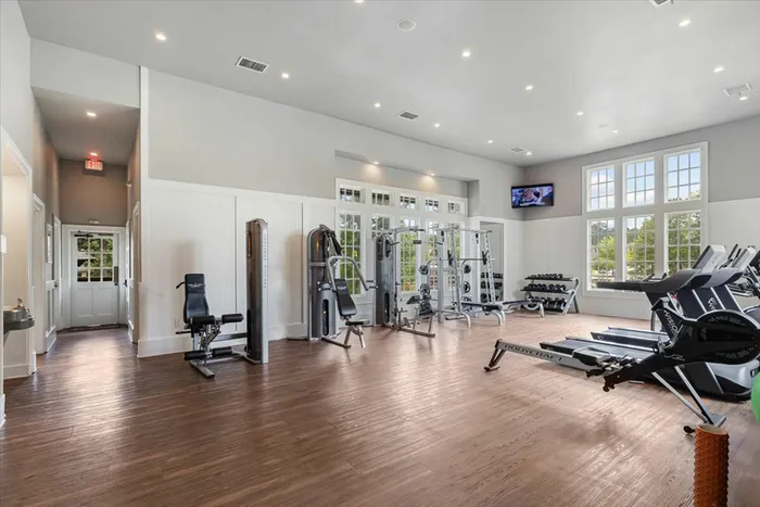 Spacious fitness center at The Cottages of Hattiesburg featuring weight machines, cardio equipment, and bright natural lighting, offering residents a convenient place to stay active.