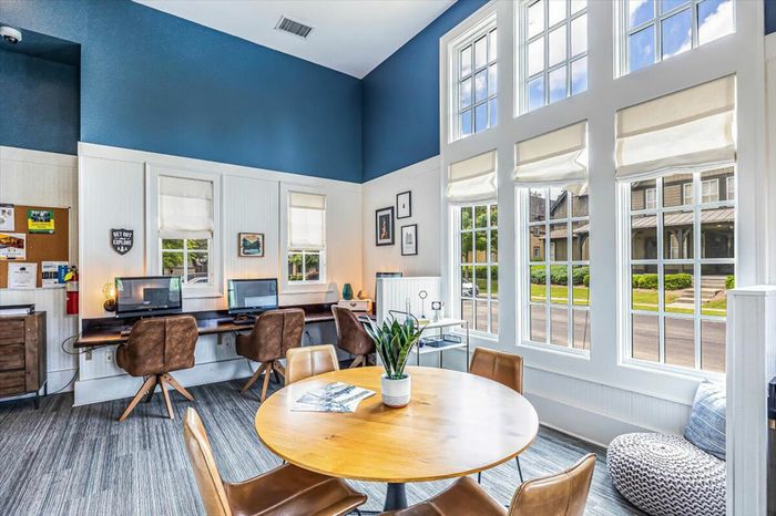 Bright and spacious community workspace at The Cottages of Hattiesburg, featuring computer stations, comfortable seating, and large windows with natural light. Perfect for studying and collaboration.