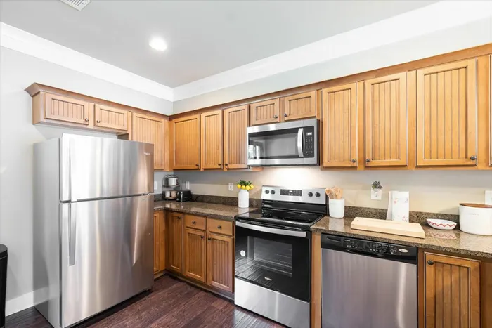 Spacious kitchen at The Cottages of Hattiesburg featuring stainless steel appliances, wood cabinets, and granite countertops.