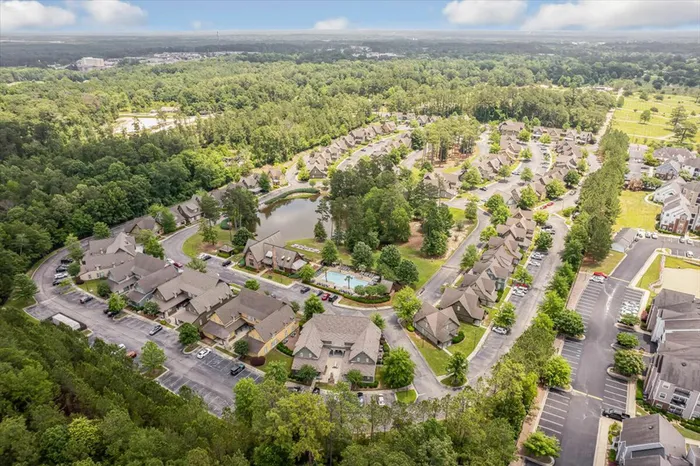 Aerial view of The Cottages of Hattiesburg community, featuring cottage-style apartments, lush green spaces, a private lake, and a resort-style pool.