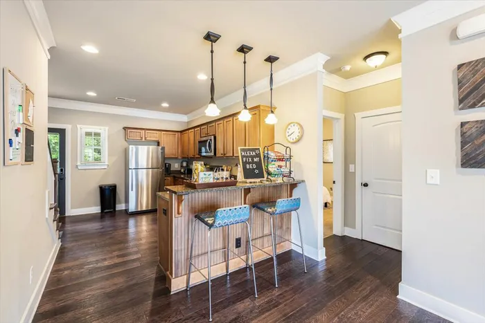 Bright and open kitchen at The Cottages of Hattiesburg featuring bar seating, stainless steel appliances, and modern lighting, perfect for student living and entertaining.