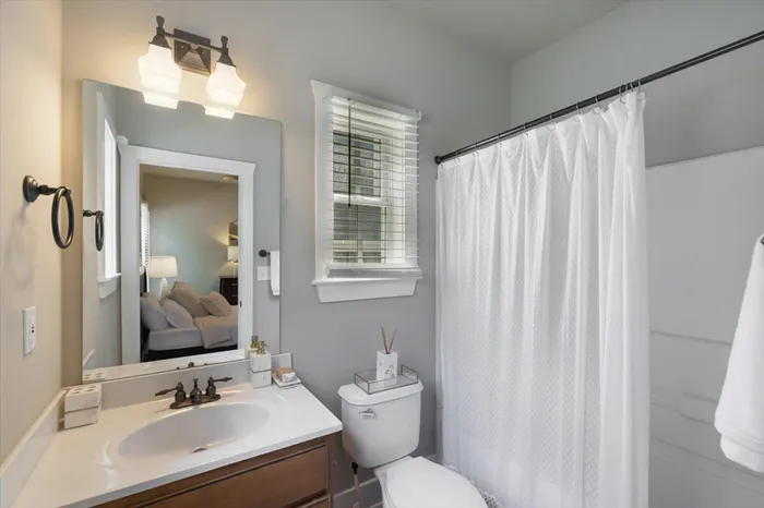 Clean and bright private bathroom at The Cottages of Hattiesburg featuring a vanity, mirror, and shower with white accents, offering a comfortable and modern living space for students.