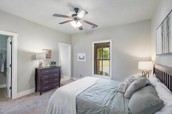 Cozy bedroom with natural light and a ceiling fan at The Cottages of Hattiesburg, featuring comfortable furnishings, soft bedding, and a walk-in closet, offering students a relaxing and private living space.